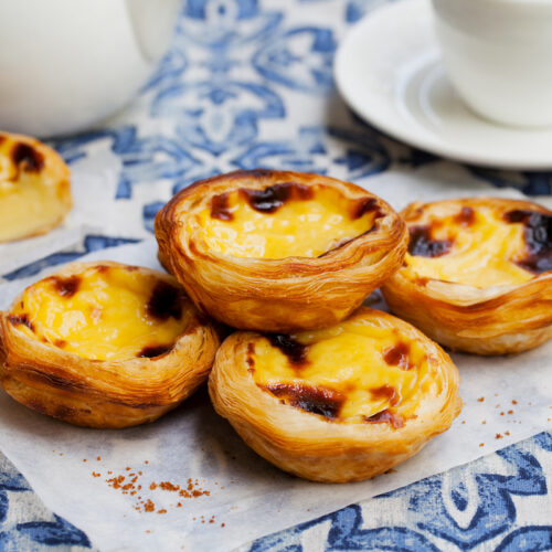 Egg tart, traditional Portuguese dessert, pastel de nata on a parchment paper. Blue background. pastel de nata